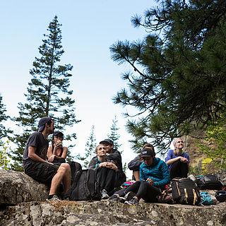 Photo of students sitting on rocks in nature underneath some trees